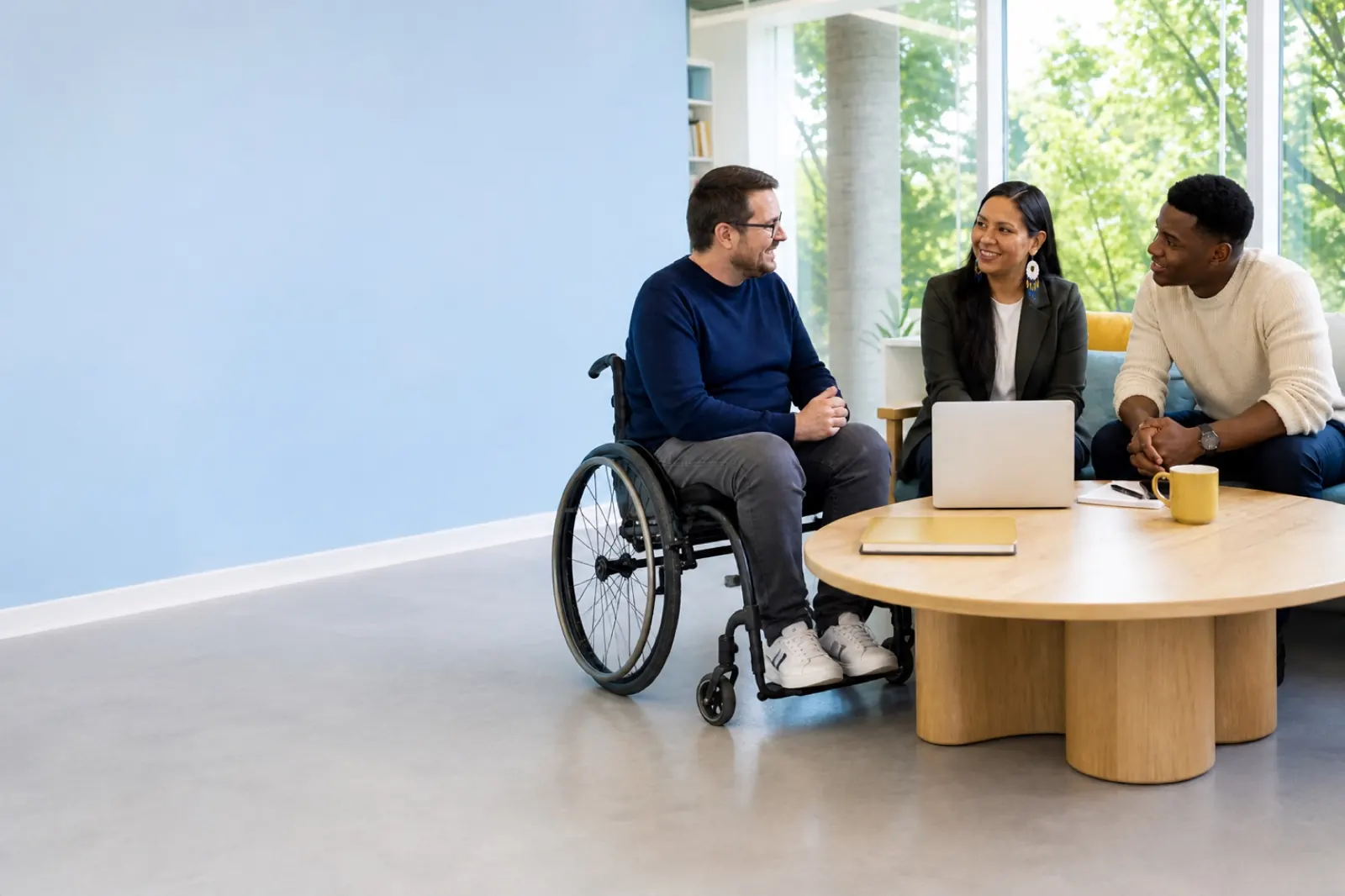 Trois personnes échangent dans un espace de travail lumineux, dont une personne en fauteuil roulant.